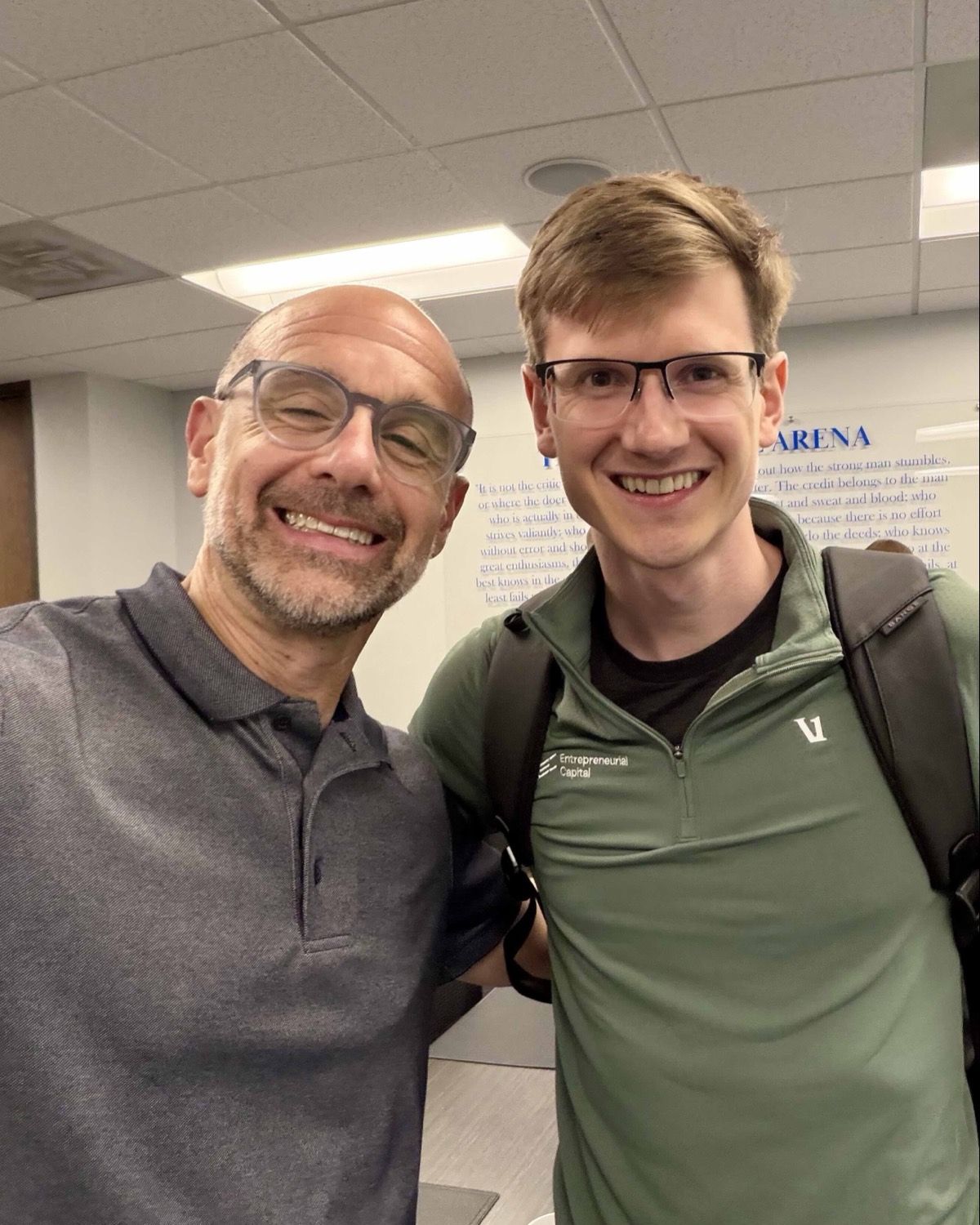 Grant Hensel and Alan Turkus smiling together in front of a wall with the Man in the Arena quote